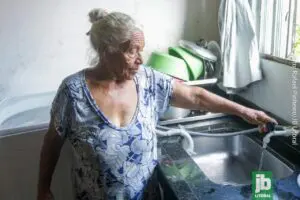 Dona Maria, de 77 anos, mora há 16 anos no bairro. Ela conta que quando chegou, não havia sequer energia elétrica. Agora, ela está esperançosa para a chegada de água tratada à região. Foto: Rafael Pinheiro/JB Litoral